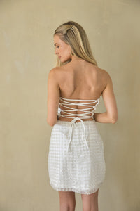 Woman wearing a white strapless top and skirt set against a beige background