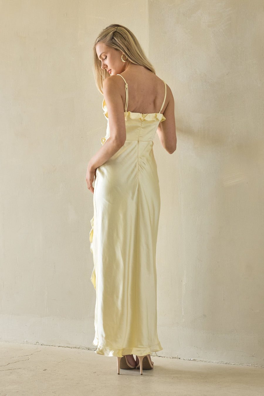 Woman in a yellow dress standing against a plain wall.