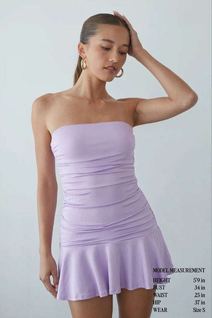 Woman wearing a light purple strapless dress against a plain background