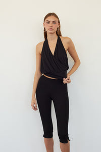 A woman modeling a black sleeveless halter-style wrap top and matching black capri leggings against a plain white studio background.