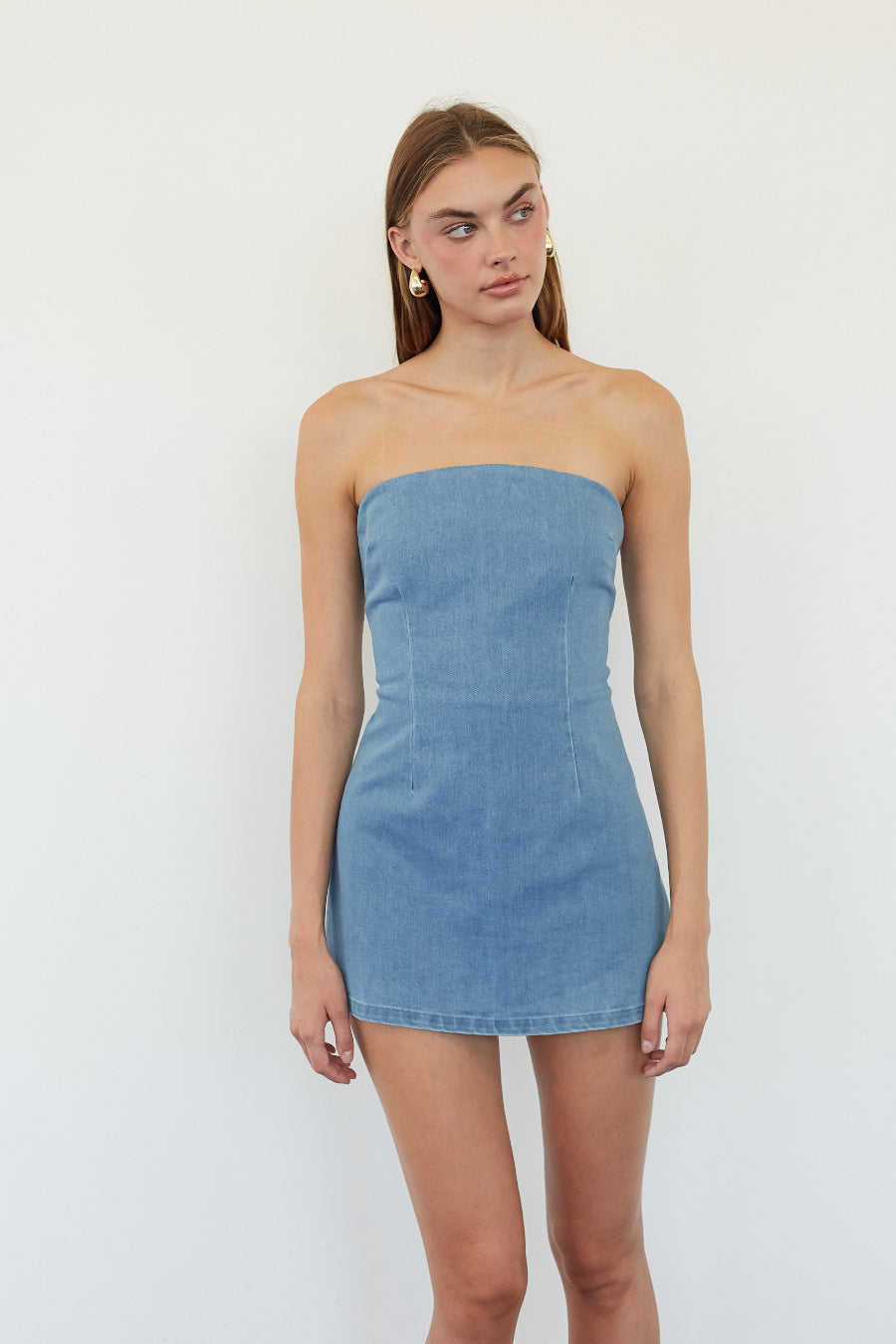 A woman modeling a strapless light blue denim mini dress against a plain white studio background.