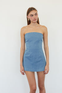 A woman modeling a strapless light blue denim mini dress against a plain white studio background.