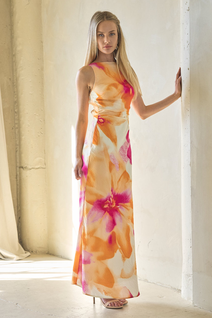 Woman wearing a floral dress standing in a bright room with white walls and curtains.