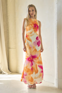 Woman wearing a floral dress standing in a bright room with curtains.