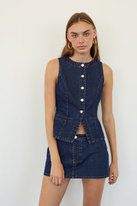 A model wearing a dark blue denim two-piece set consisting of a sleeveless button-front vest and a matching mini skirt, set against a plain white background.