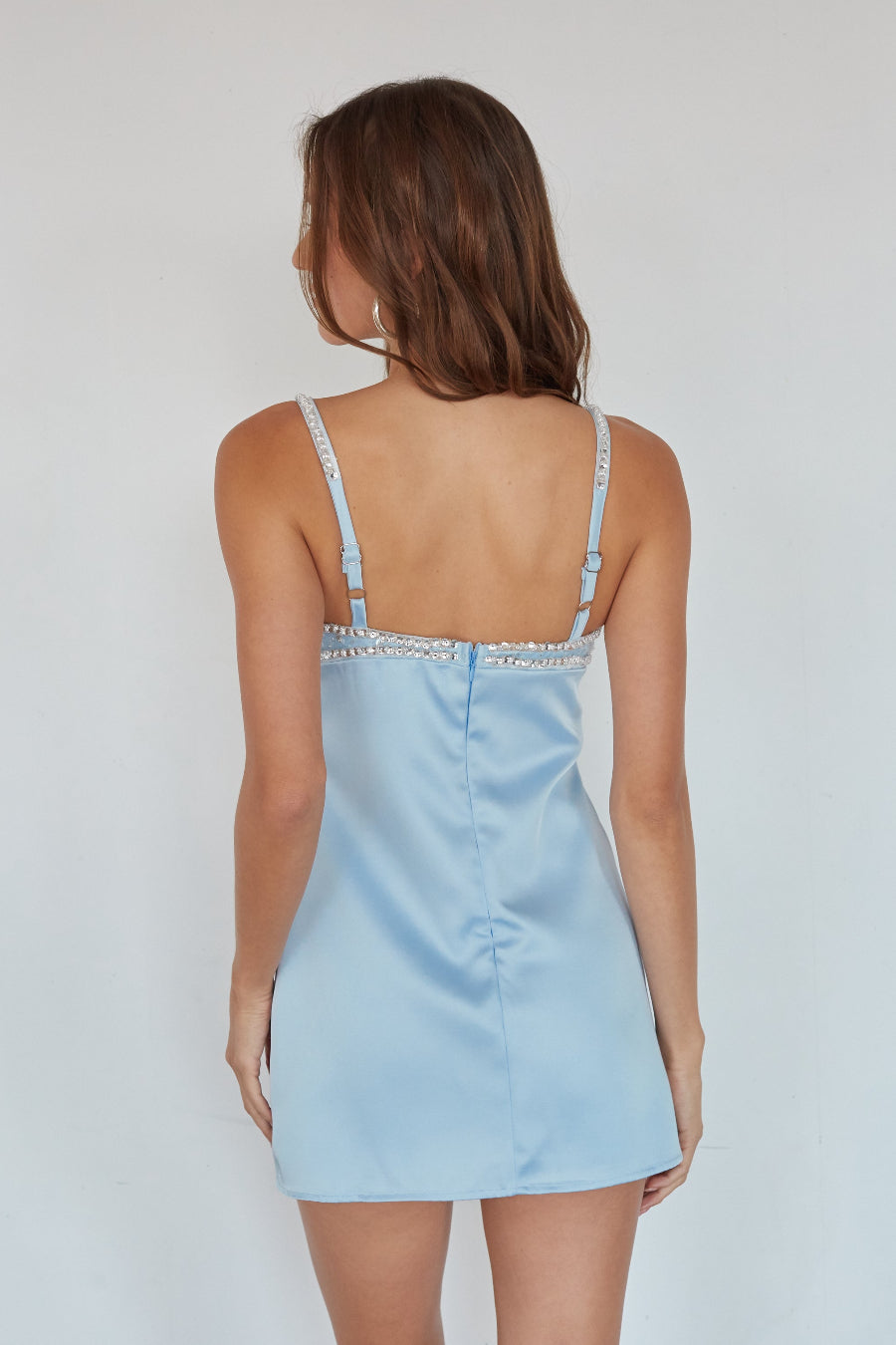 Woman wearing a light blue slip dress against a plain background