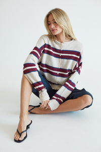 blonde model in a beige and red striped sweater, sitting on the floor behind a gray background