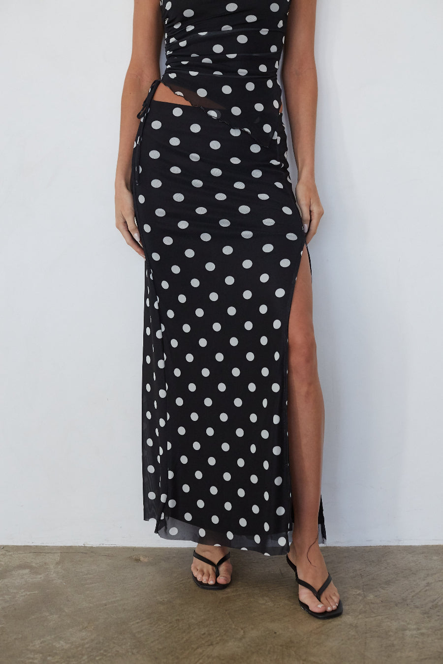 Black polka dot dress with a slit on a plain background