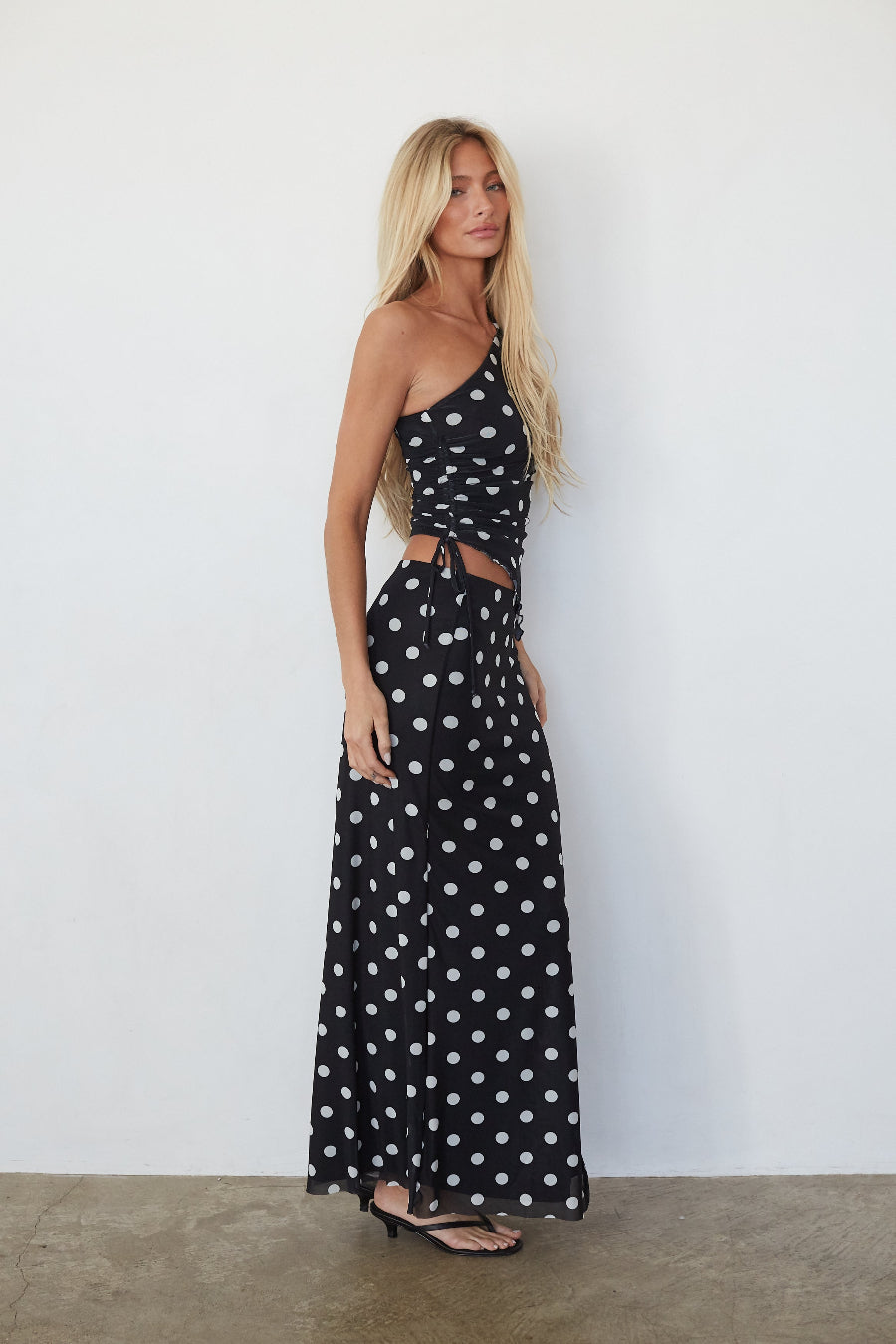 Woman wearing a black polka dot dress against a white wall