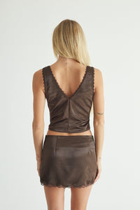 A woman shown from the back wearing a dark brown two-piece set consisting of a sleeveless crop top with a scalloped V-neckline and a matching mini skirt with a scalloped hem, against a plain light gray background.
