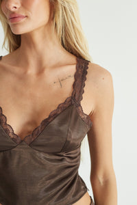 A blonde model wearing a dark brown satin top with lace trim.