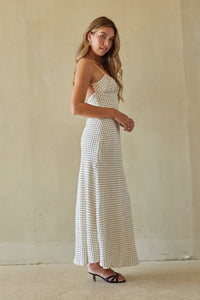 Woman wearing a white patterned dress standing against a plain wall.