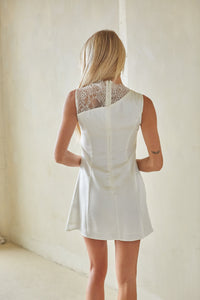 Woman wearing a white dress with lace detailing in a minimal indoor setting
