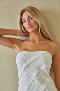 Woman wearing a white strapless dress against a beige background