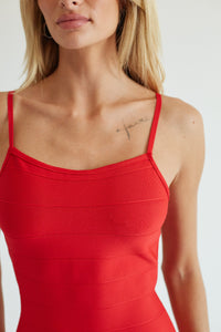 A close-up of a model wearing a bright red ribbed spaghetti-strap camisole top against a plain light background.
