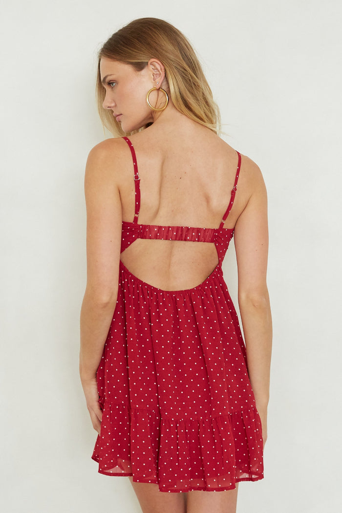 Woman wearing a red polka dot dress with cut-out back on a white background