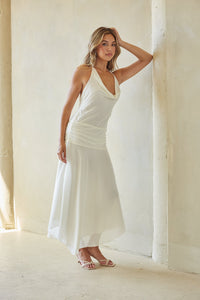 Woman in a white dress standing against a light-colored wall.