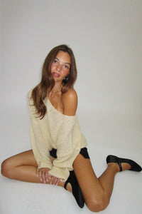 Woman posing in a beige sweater and black pants on a white background