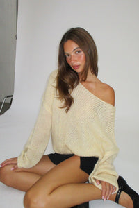 Woman wearing a beige sweater and black underwear against a plain background