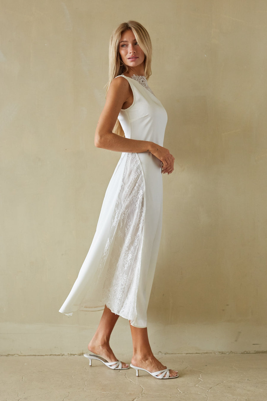 Woman wearing a white dress standing against a beige wall.
