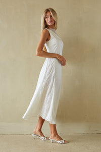 Woman wearing a white dress standing against a beige wall.