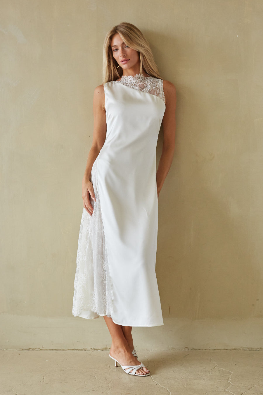 Woman wearing a white dress with lace details against a beige wall.