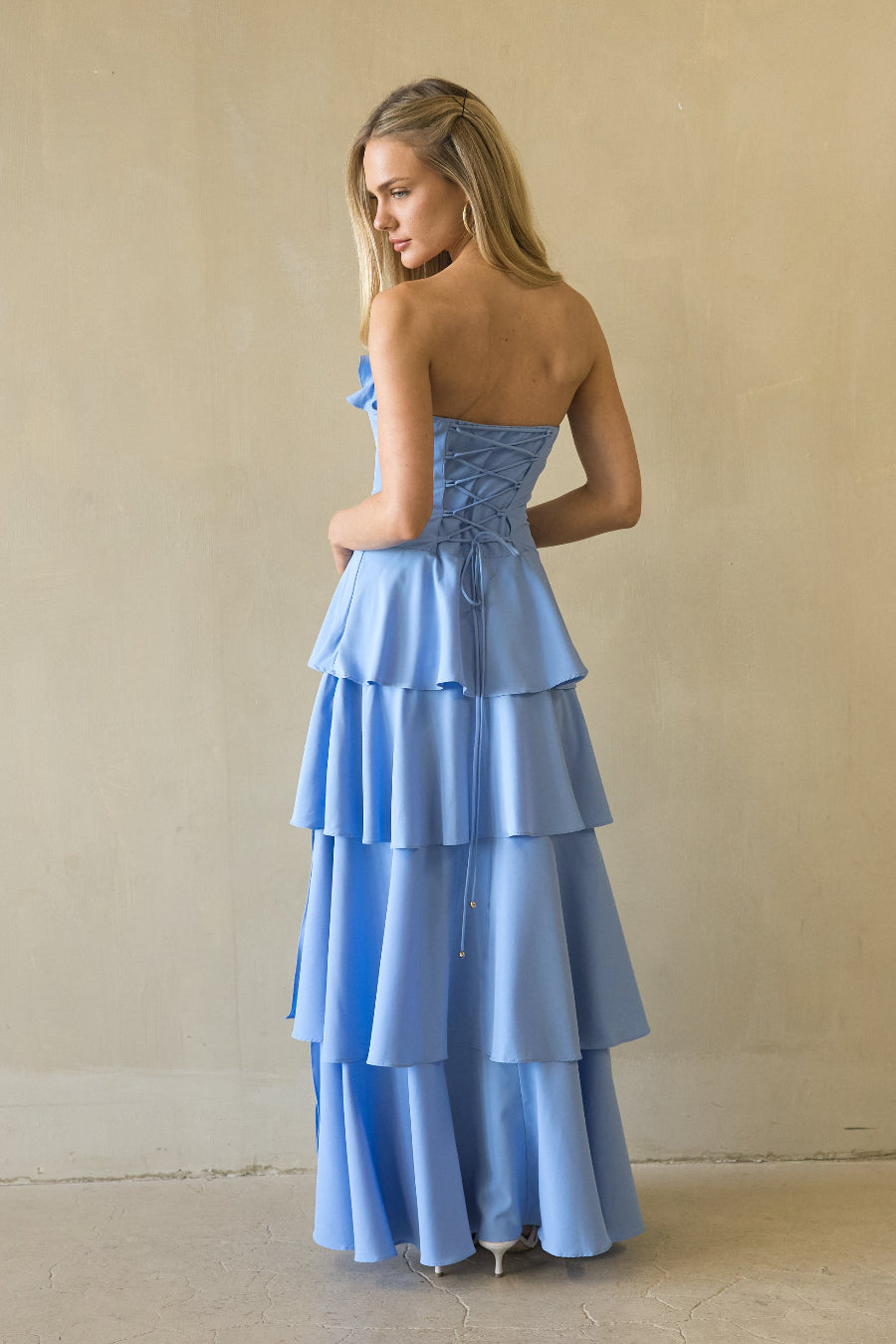 Woman wearing a light blue strapless, tiered dress against a plain background