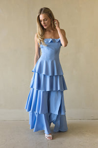 blue-image | Woman wearing a blue dress with ruffled layers against a beige wall.