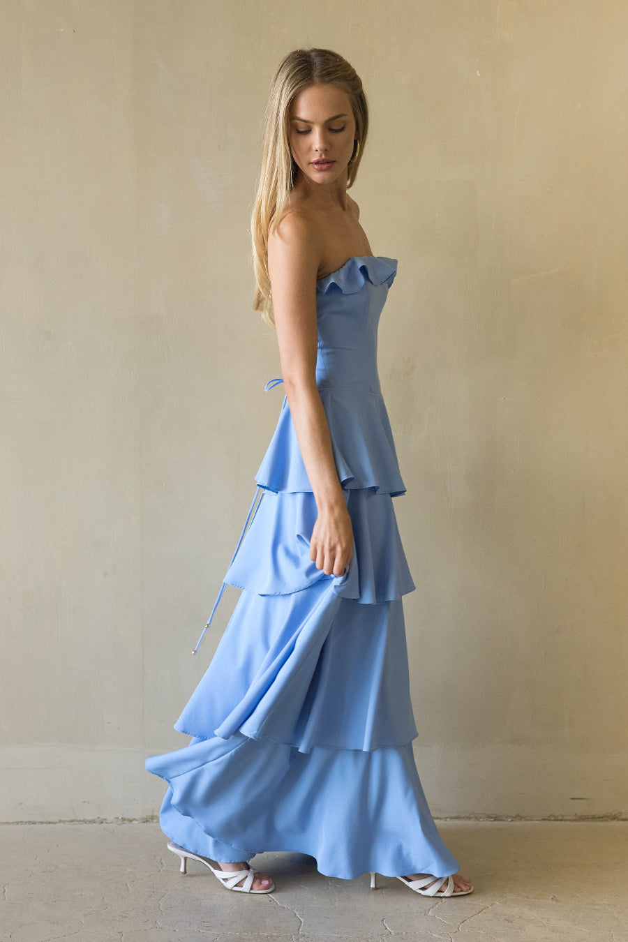Woman wearing a blue strapless dress with ruffled layers against a plain background