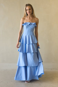 blue-image | Woman wearing a light blue strapless gown with ruffled layers against a plain background