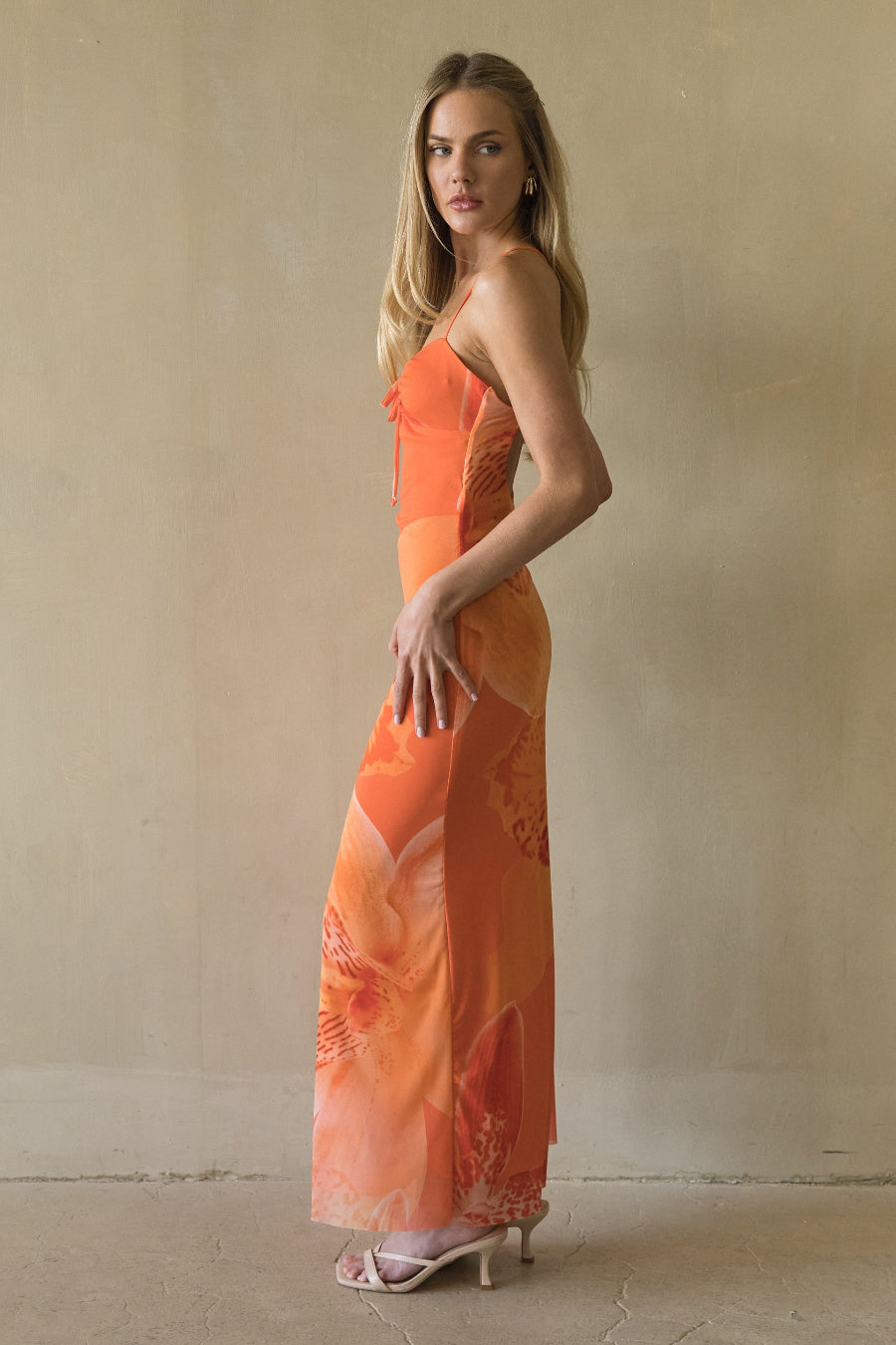 Woman wearing an orange dress with floral patterns against a plain background