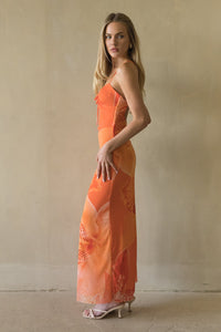 Woman wearing an orange dress with floral patterns against a plain background