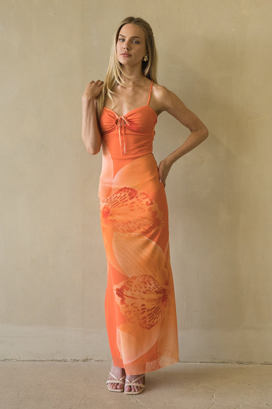 Woman wearing an orange dress with shell patterns against a plain background