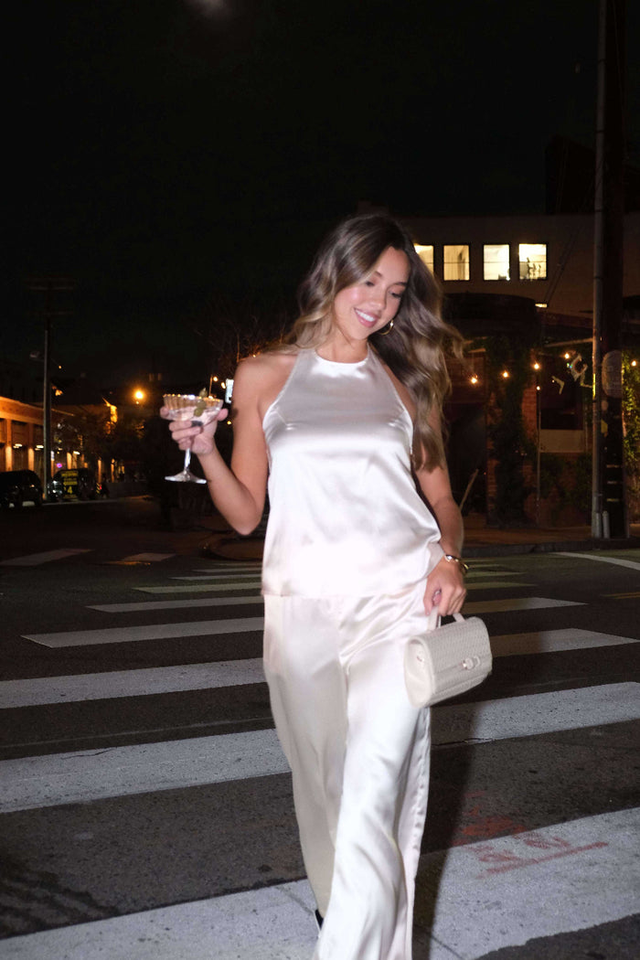 Woman in a white satin dress crossing a street at night.