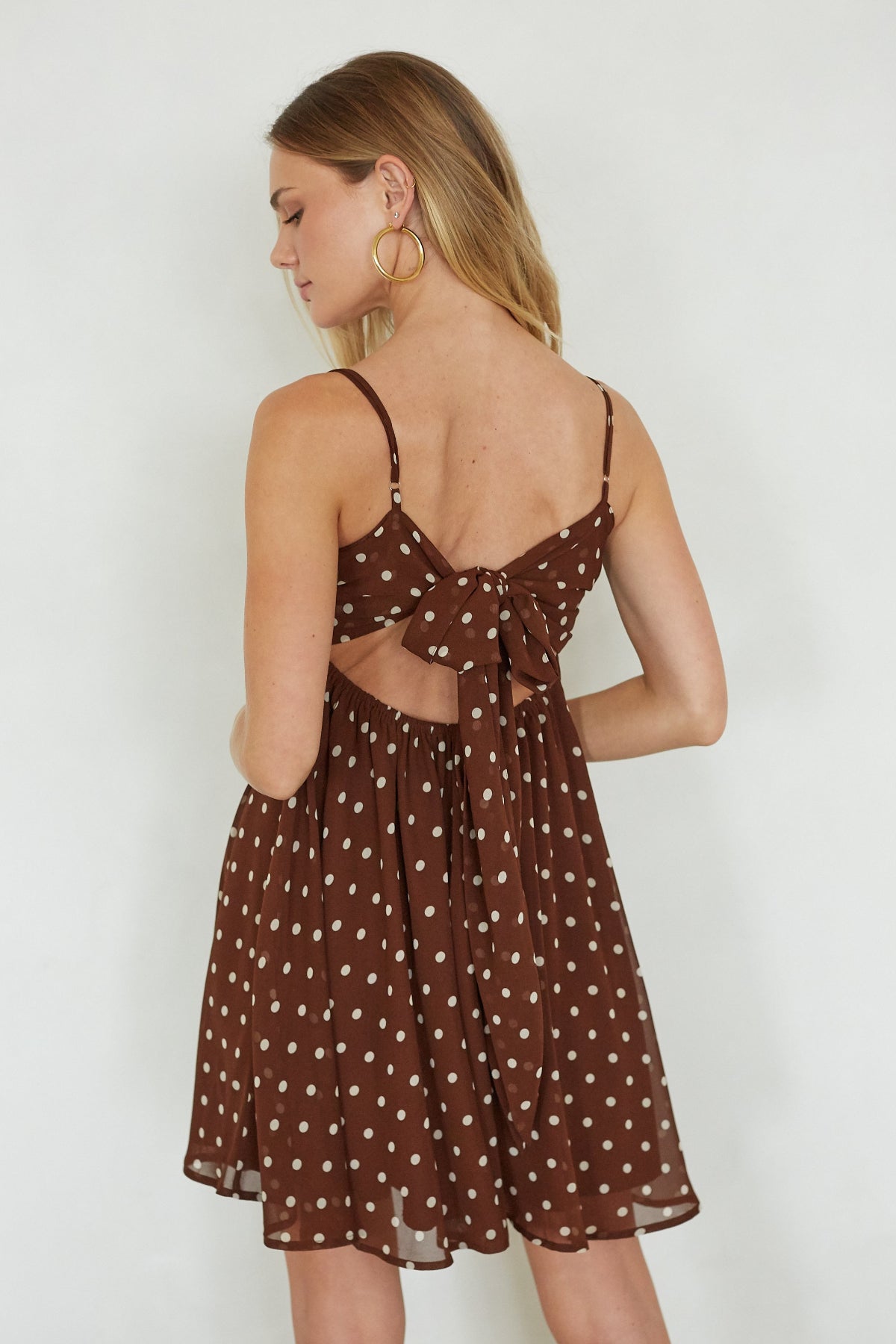 Woman wearing a brown polka dot dress with thin straps on a white background