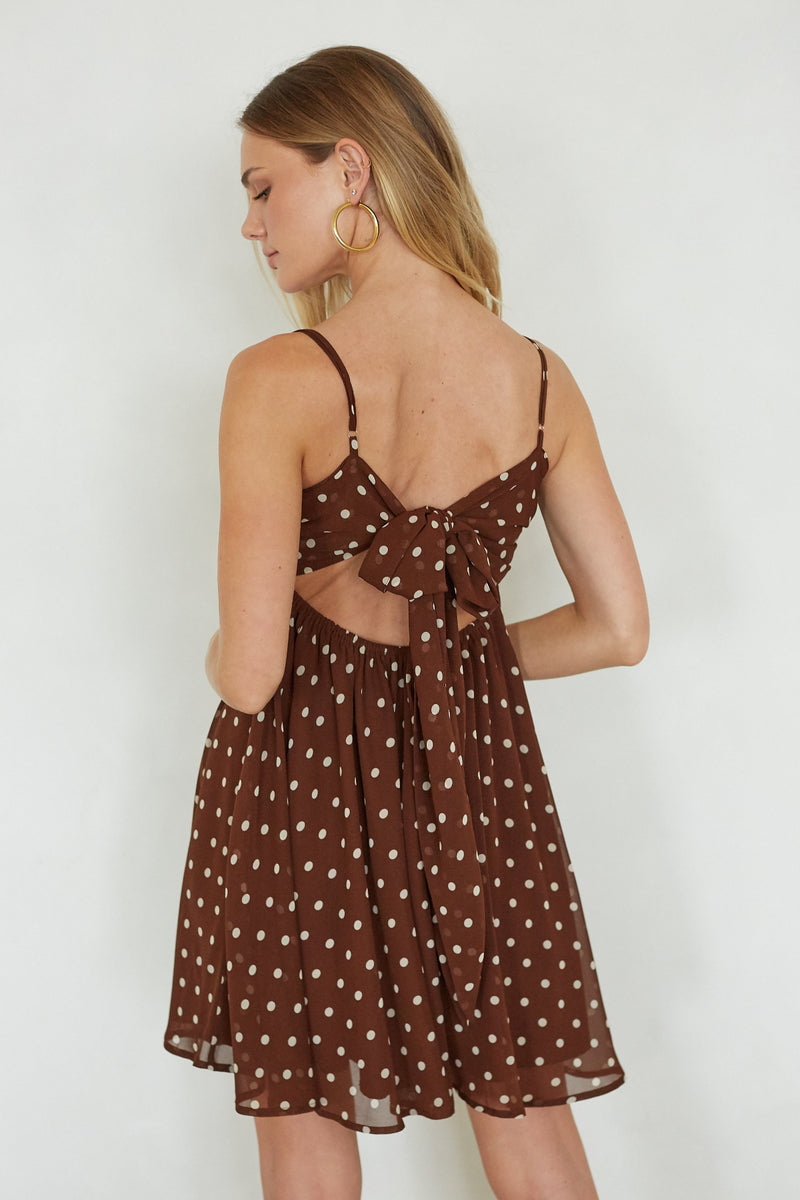 Woman wearing a brown polka dot dress with thin straps on a white background