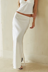 Woman wearing a white patterned outfit standing against a beige wall.