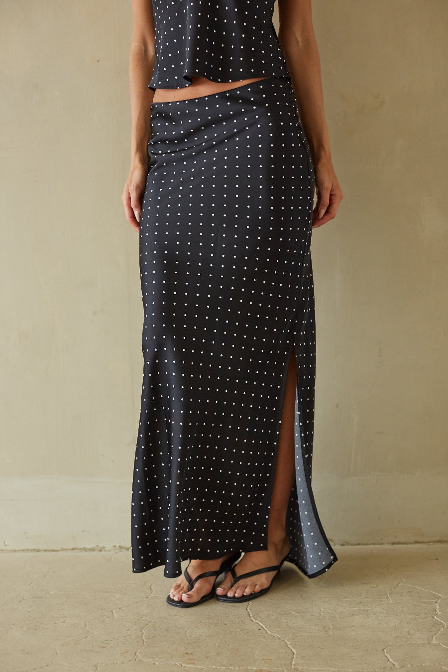 Person wearing a black polka dot skirt with a plain background