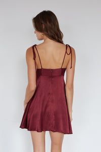 Woman wearing a burgundy dress with thin straps on a plain background