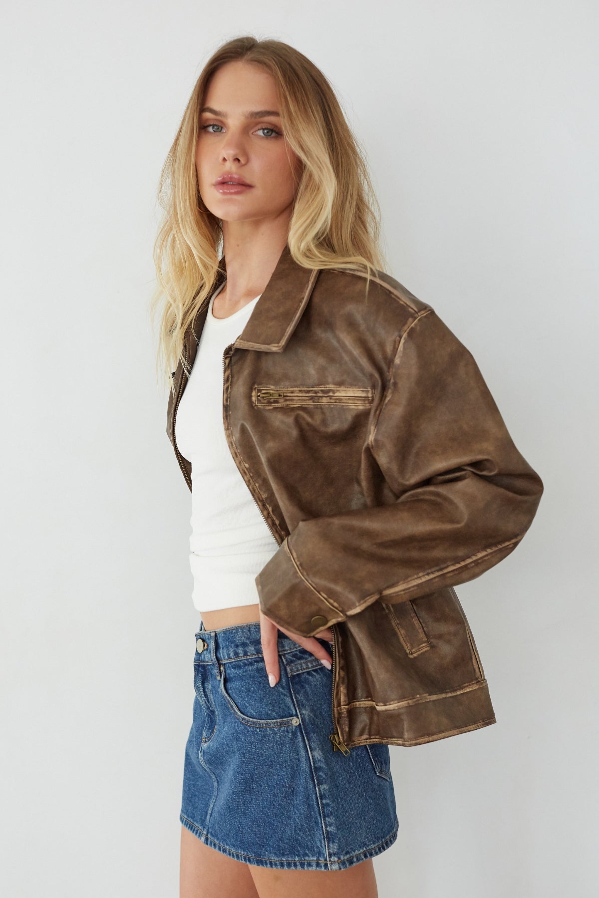 Woman wearing a brown jacket, white top, and denim shorts against a white background