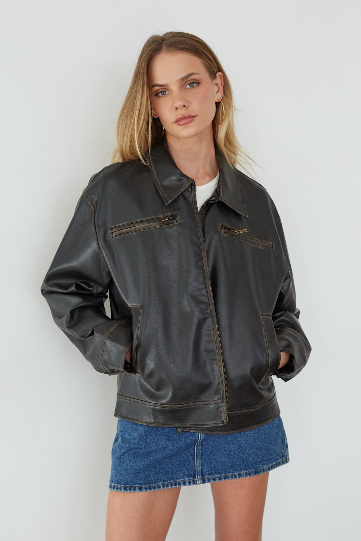 Woman wearing a black leather jacket and denim skirt against a white background