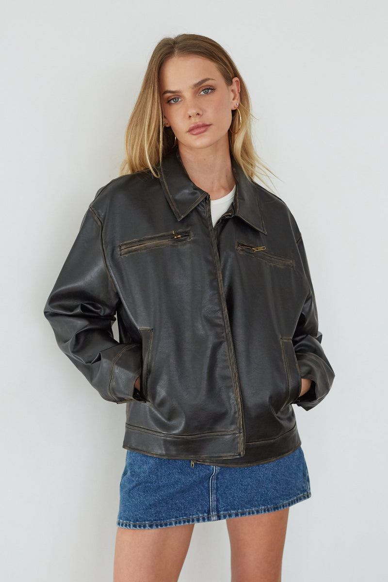 Woman wearing a black leather jacket and denim skirt against a white background