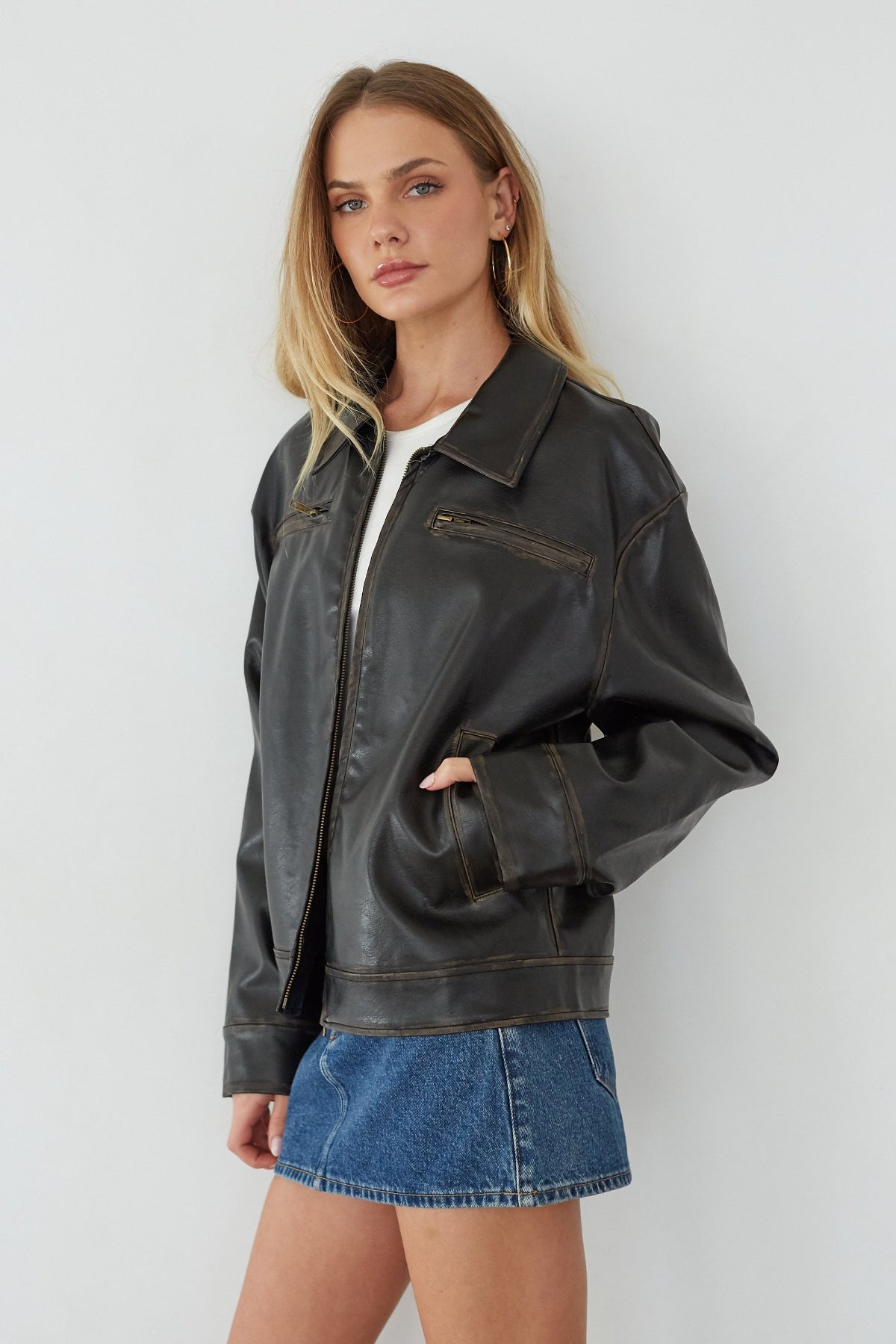 Woman wearing a black leather jacket and denim skirt against a white background