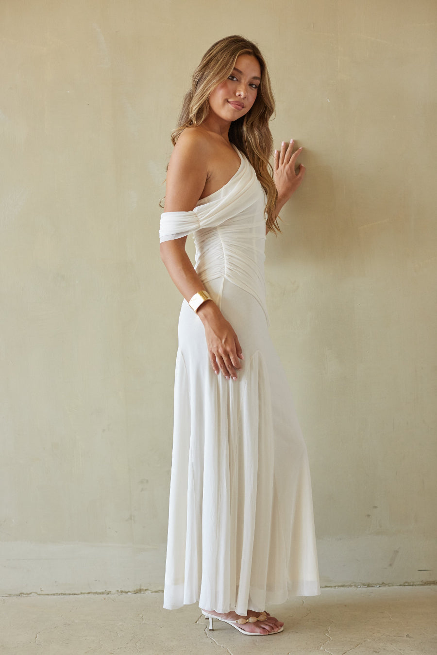 Woman wearing a white off-shoulder dress against a plain wall.