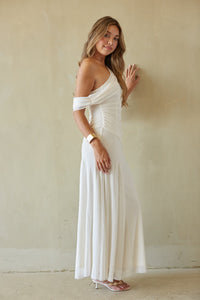 Woman wearing a white off-shoulder dress against a plain wall.