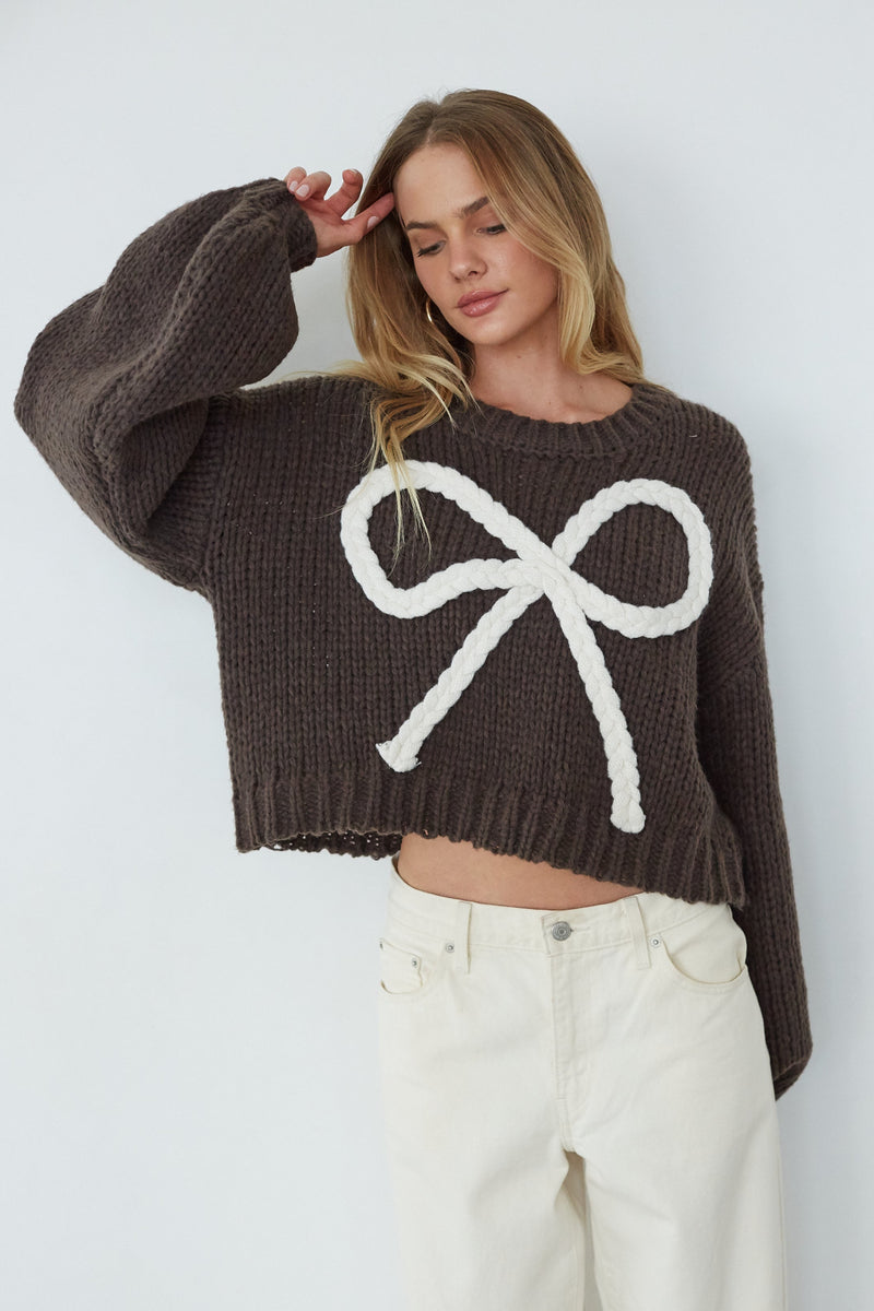 Woman wearing a brown sweater with a white bow design against a white background