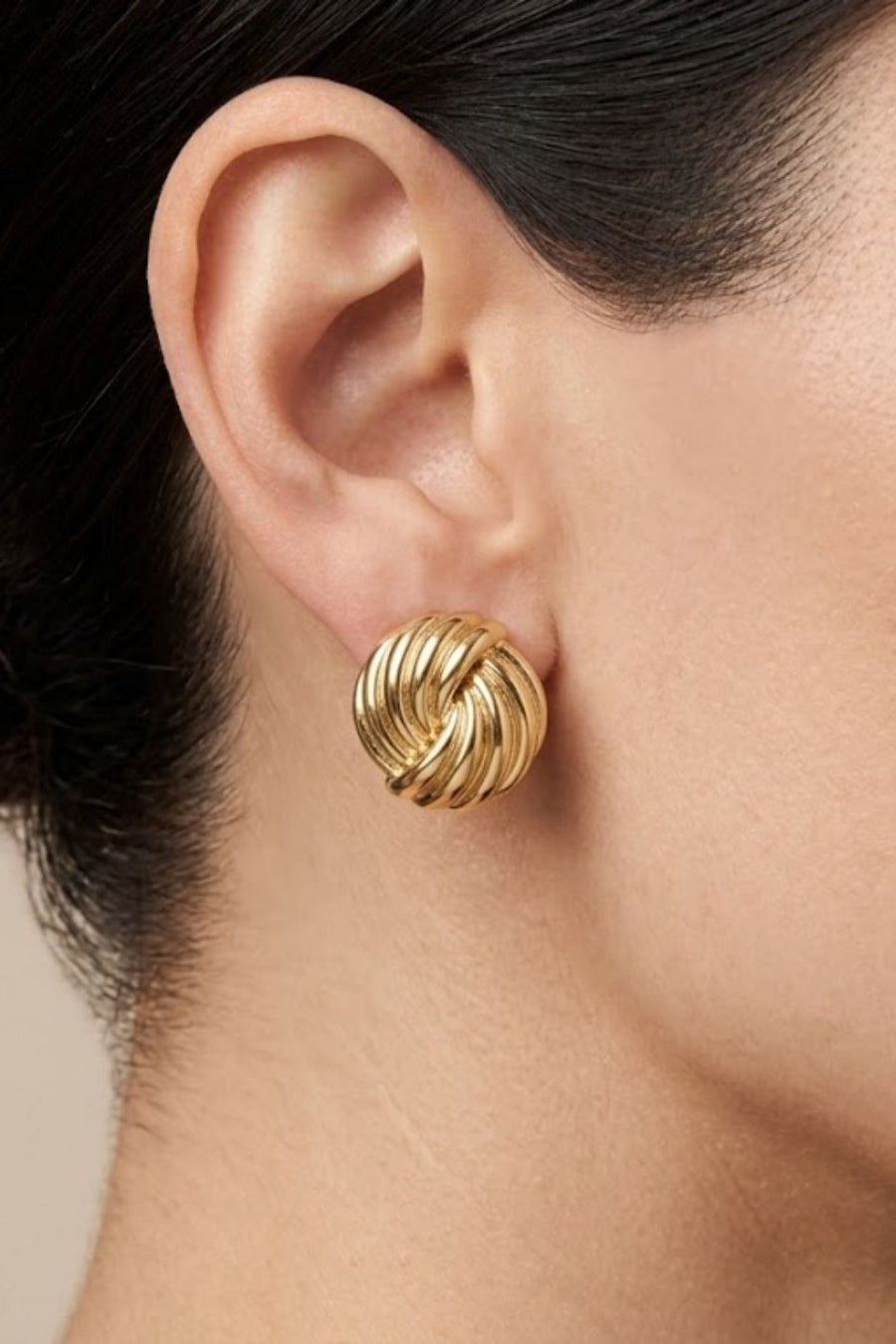 A close-up of a model's ear wearing a textured, twisted gold post earring.