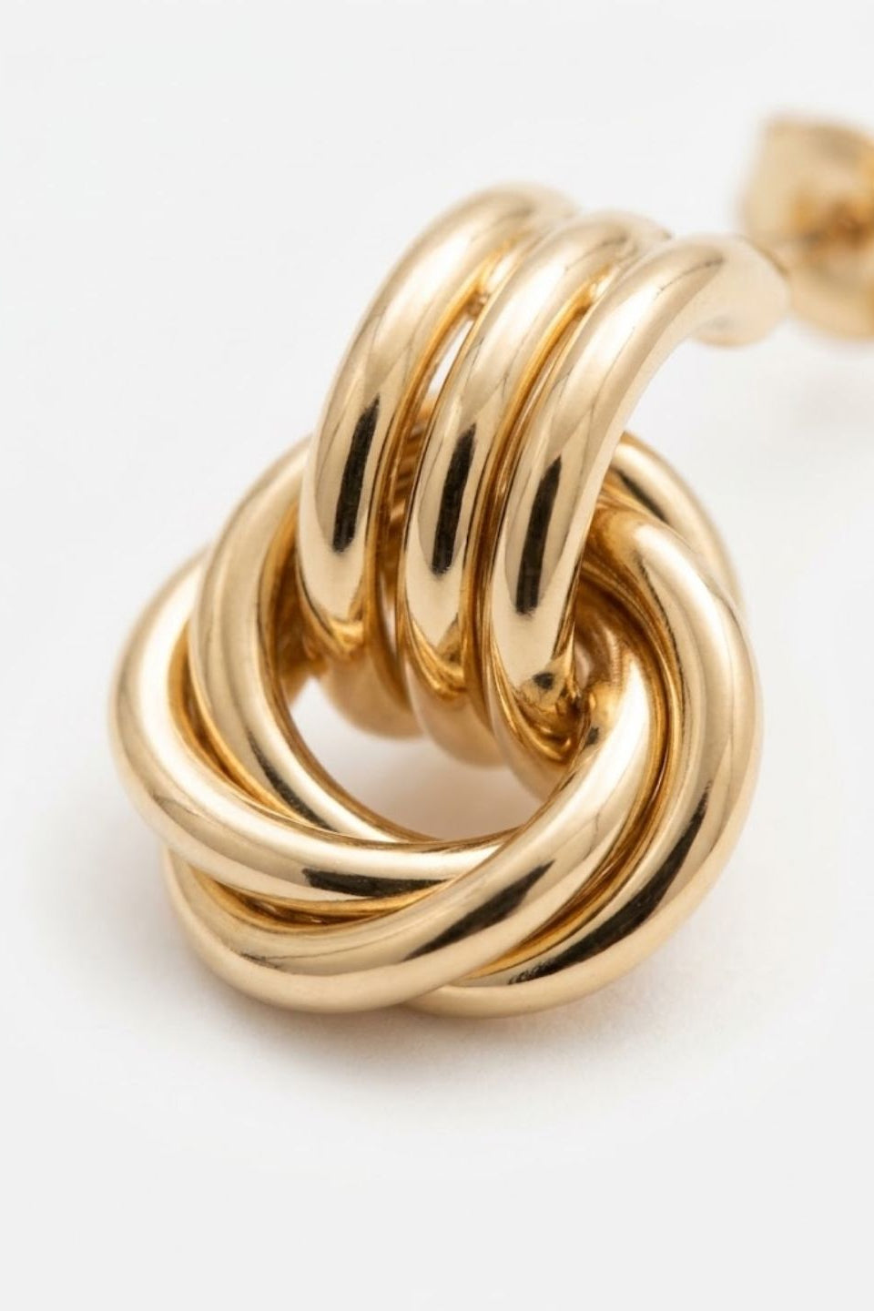 A close-up of a polished gold knot stud earring on a clean white background.
