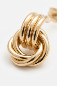 A close-up of a polished gold knot stud earring on a clean white background.