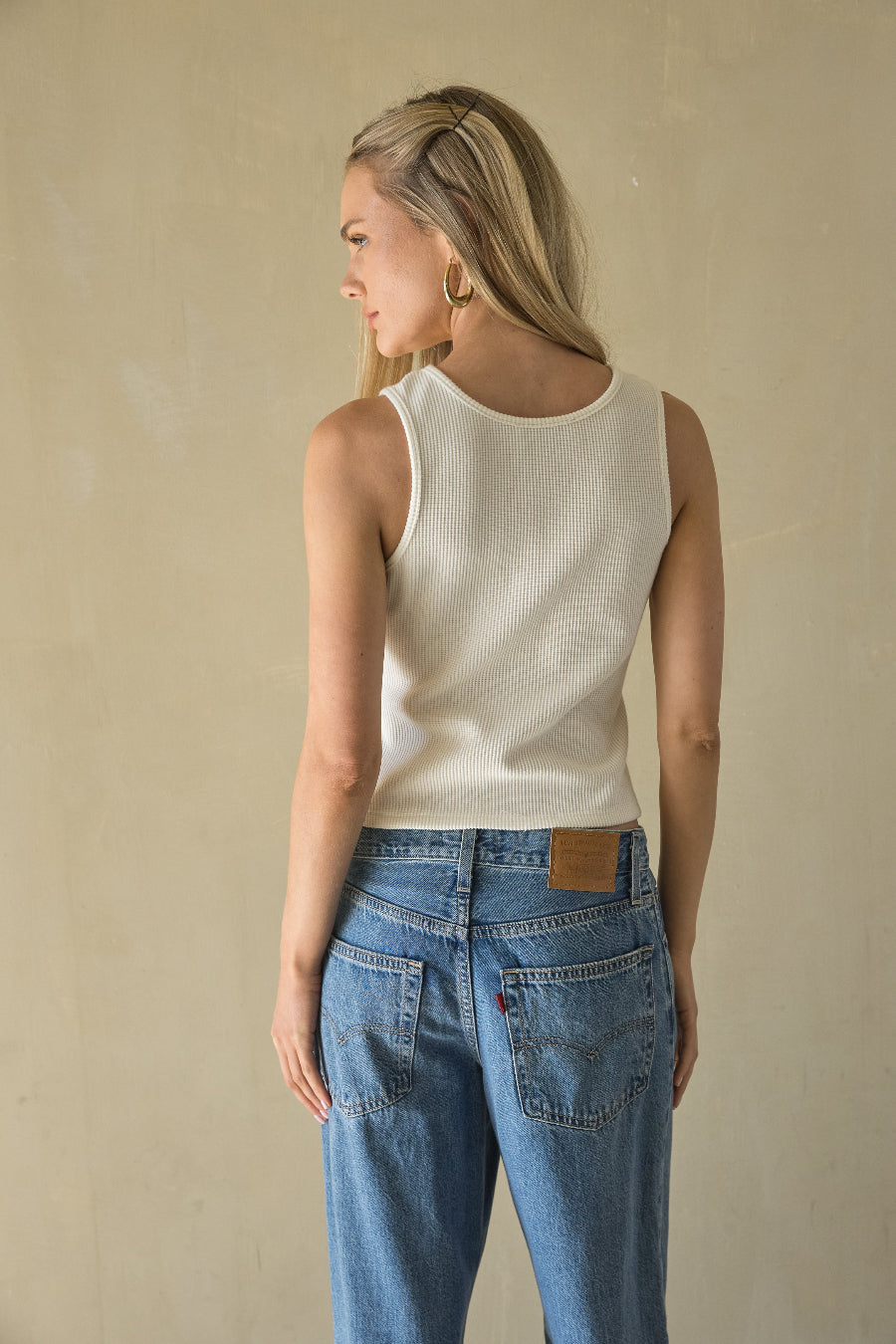 Woman wearing a white sleeveless top and blue jeans against a beige background